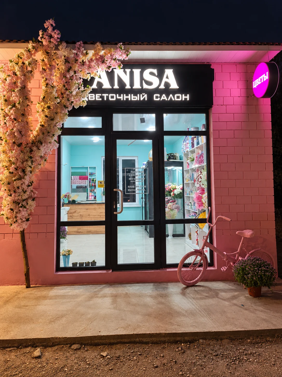 Фасад Anisa: розовая кирпичная стена, цветочная арка и стеклянный вход с вывеской